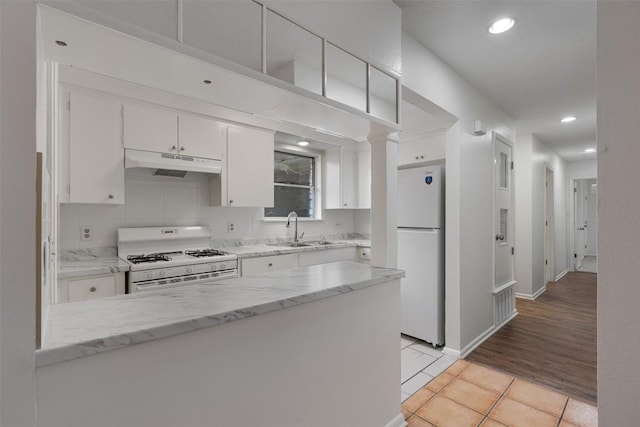 2616 Audubon Pl, Austin, TX 78741 - kitchen with white appliances, under cabinet range hood, white cabinets, light tile patterned flooring, and tasteful backsplash
