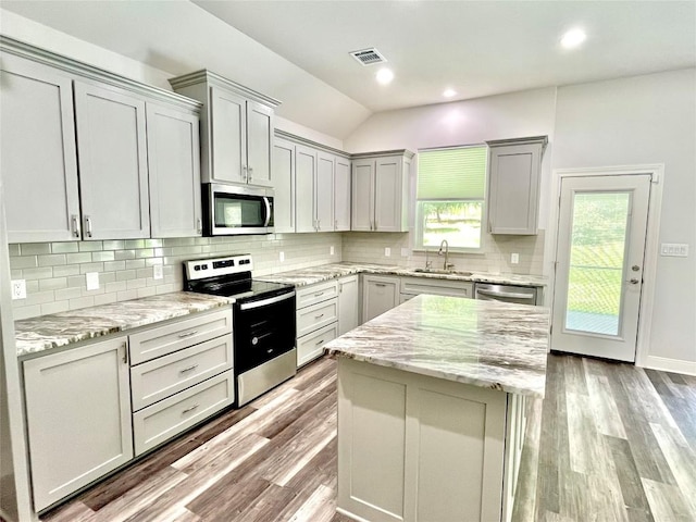 108 W Keamuku Ct, Bastrop, TX 78602 - kitchen with stainless steel appliances, light wood-style floors, backsplash, gray cabinetry, and light stone countertops
