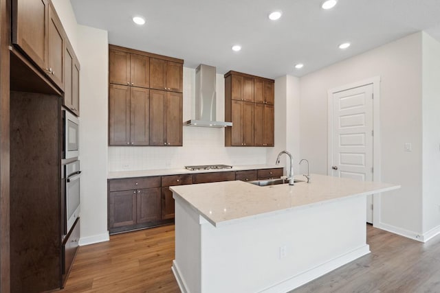 1754 Sawmill Xing, Round Rock, TX 78665 - kitchen with wall chimney exhaust hood, stainless steel appliances, light wood-style floors, backsplash, and a center island with sink