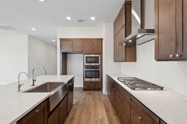 1754 Sawmill Xing, Round Rock, TX 78665 - kitchen featuring appliances with stainless steel finishes, wall chimney exhaust hood, light stone counters, light wood-type flooring, and recessed lighting