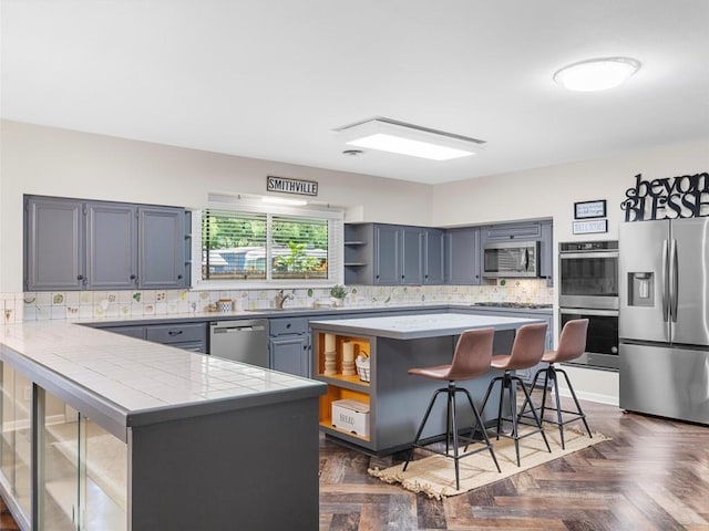kitchen featuring appliances with stainless steel finishes, open shelves, a breakfast bar area, a peninsula, and backsplash