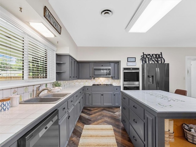 kitchen with stainless steel appliances, gray cabinetry, open shelves, tile counters, and tasteful backsplash