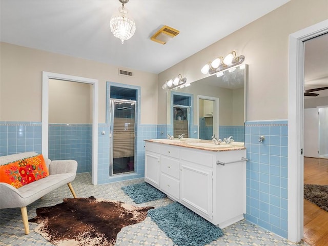 bathroom with tile walls, a wainscoted wall, double vanity, and a shower stall