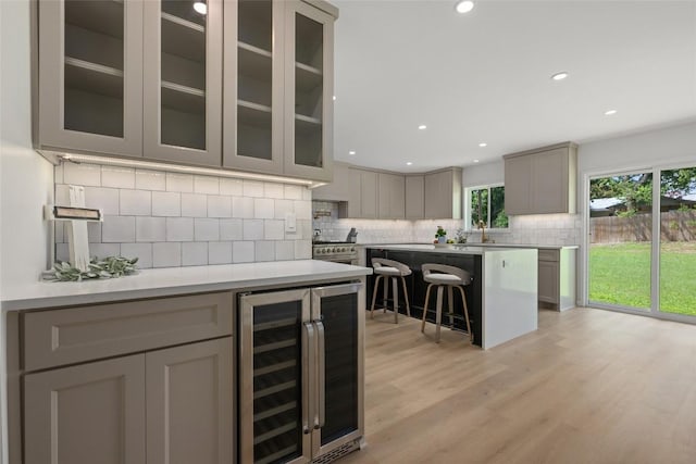 1101 Floradale Dr, Austin, TX 78753 - kitchen featuring wine cooler, a breakfast bar area, gray cabinetry, tasteful backsplash, and glass insert cabinets