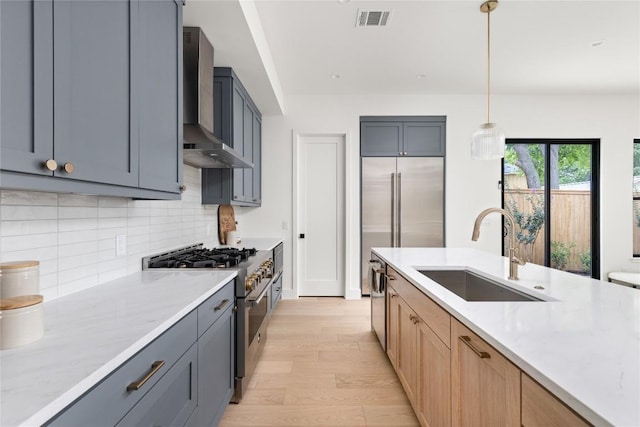 1703 Madison, Austin, TX 78757 - kitchen featuring high end stainless steel range, wall chimney exhaust hood, tasteful backsplash, light wood-type flooring, and pendant lighting