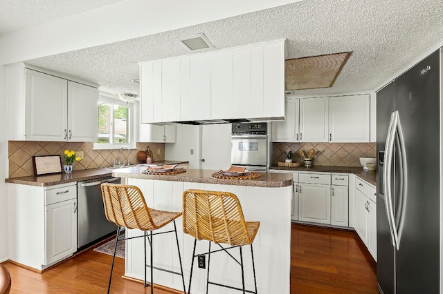 4009 Cordova Dr, Austin, TX 78759 - kitchen featuring appliances with stainless steel finishes, a textured ceiling, dark wood-style floors, dark countertops, and a breakfast bar area