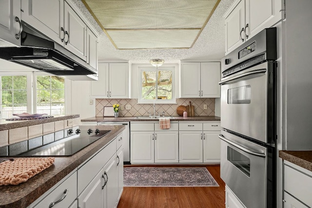 4009 Cordova Dr, Austin, TX 78759 - kitchen with black electric cooktop, double oven, extractor fan, dark countertops, and dark wood-type flooring