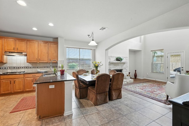 1802 Misty Ridge Dr, Leander, TX 78641 - kitchen featuring under cabinet range hood, backsplash, a stone fireplace, stainless steel cooktop, and dark stone countertops