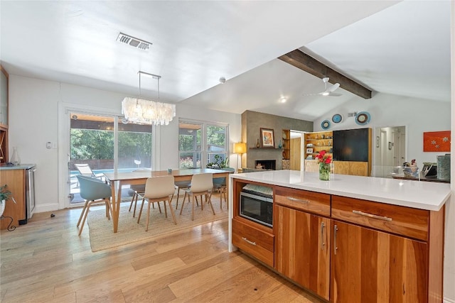 1407 Spring Gdn, Austin, TX 78746 - kitchen with stainless steel microwave, light wood-style flooring, a fireplace, light countertops, and brown cabinets