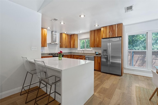 1407 Spring Gdn, Austin, TX 78746 - kitchen featuring stainless steel appliances, wall chimney range hood, brown cabinets, a breakfast bar, and light wood-style floors