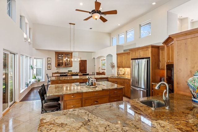 27 Stillmeadow Dr, The Hills, TX 78738 - kitchen featuring freestanding refrigerator, brown cabinets, a towering ceiling, a peninsula, and arched walkways