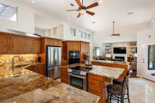 27 Stillmeadow Dr, The Hills, TX 78738 - kitchen with black appliances, a ceiling fan, brown cabinetry, a high ceiling, and a center island