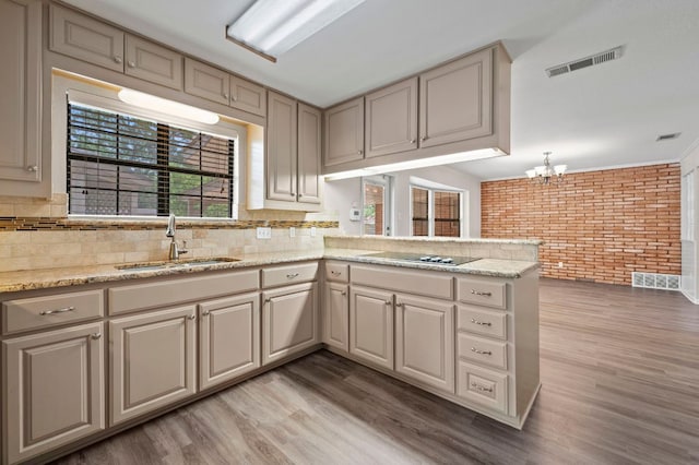 11705 Oak Trl, Austin, TX 78753 - kitchen featuring brick wall, black electric cooktop, light wood-style floors, a chandelier, and tasteful backsplash
