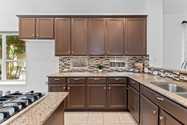 13121 Armaga Springs Rd, Austin, TX 78727 - kitchen featuring decorative backsplash, stainless steel gas cooktop, light tile patterned floors, light stone counters, and dark brown cabinetry