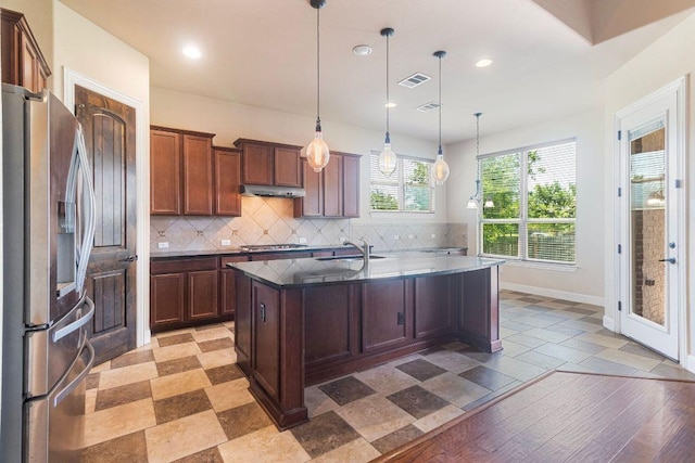 2713 Windy Vane Dr, Pflugerville, TX 78660 - kitchen with stainless steel appliances, under cabinet range hood, tasteful backsplash, a center island with sink, and hanging light fixtures
