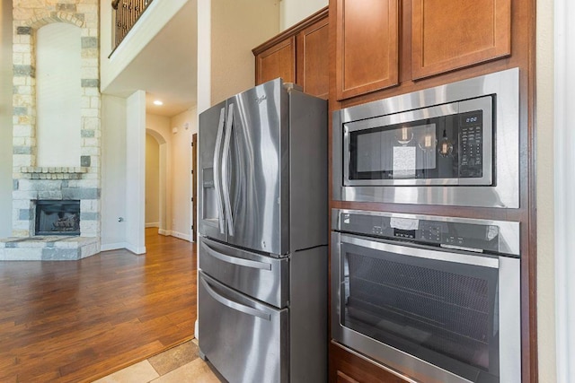 2713 Windy Vane Dr, Pflugerville, TX 78660 - kitchen with stainless steel appliances, brown cabinets, arched walkways, a stone fireplace, and wood finished floors