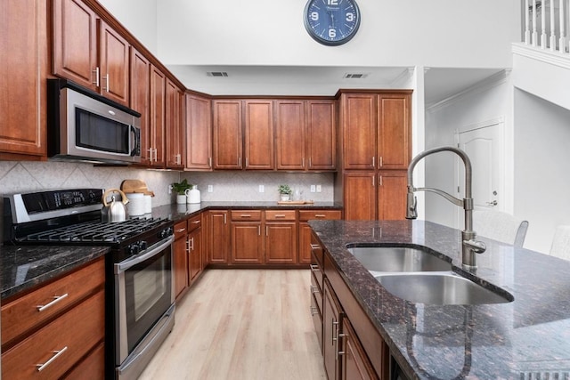 6715 Windrift Way Unit 29, Austin, TX 78745 - kitchen with appliances with stainless steel finishes, light wood-style flooring, decorative backsplash, dark stone countertops, and crown molding