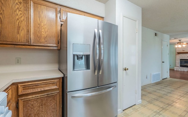 5605 China Berry Rd, Austin, TX 78744 - kitchen with stainless steel fridge with ice dispenser, light countertops, brown cabinets, light flooring, and a fireplace