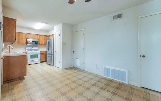 5605 China Berry Rd, Austin, TX 78744 - kitchen featuring appliances with stainless steel finishes, light countertops, brown cabinetry, light floors, and ceiling fan