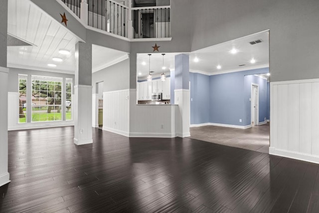 607 County Cork Ln, Leander, TX 78641 - unfurnished living room with wainscoting, a towering ceiling, dark wood finished floors, crown molding, and a decorative wall
