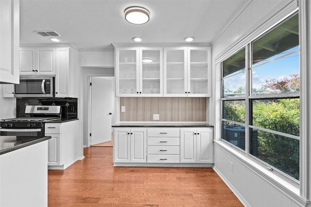 2601 Ashdale Dr, Austin, TX 78757 - kitchen with stainless steel appliances, dark countertops, white cabinets, glass insert cabinets, and light wood-style flooring