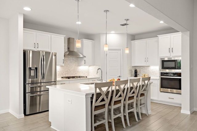 16713 Elsinore Ln, Pflugerville, TX 78660 - kitchen with stainless steel appliances, wall chimney exhaust hood, a center island with sink, backsplash, and light wood finished floors