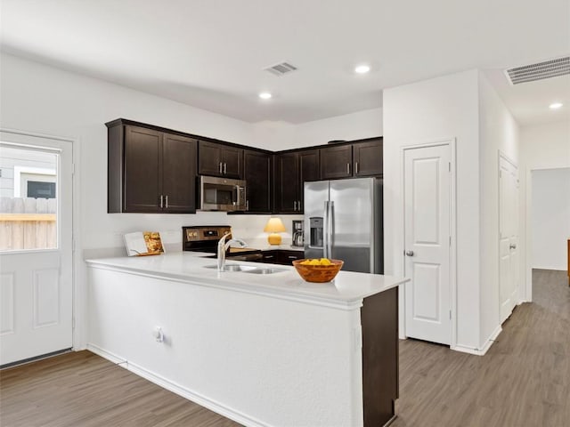 308 Sunfish Ln, Bastrop, TX 78602 - kitchen with appliances with stainless steel finishes, light wood-type flooring, light countertops, dark brown cabinetry, and a peninsula