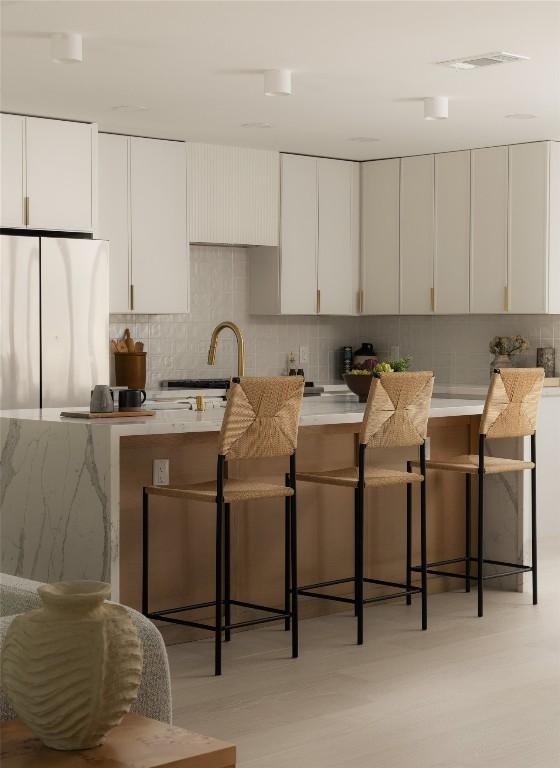 1206 Cloverleaf Dr, Austin, TX 78723 - kitchen with freestanding refrigerator, decorative backsplash, a kitchen breakfast bar, and white cabinets