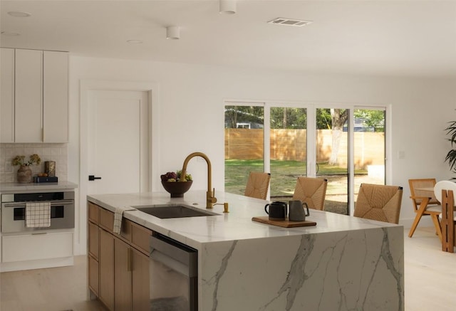 1206 Cloverleaf Dr, Austin, TX 78723 - kitchen with appliances with stainless steel finishes, a kitchen island with sink, light stone counters, tasteful backsplash, and modern cabinets