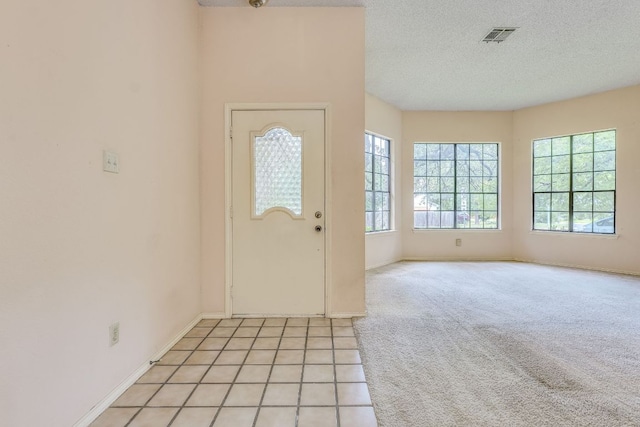 13102 Amarillo Ave, Austin, TX 78729 - foyer entrance with healthy amount of natural light, a textured ceiling, light tile patterned flooring, and light carpet