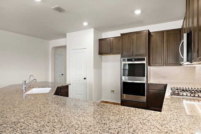 4669 Padula Dr, Round Rock, TX 78665 - kitchen with appliances with stainless steel finishes, dark brown cabinets, light stone counters, tasteful backsplash, and recessed lighting