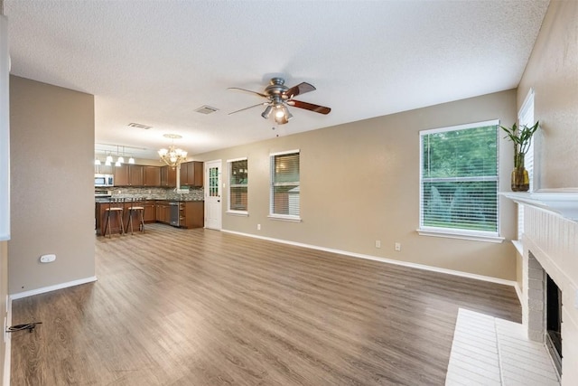 16504 Jadestone Dr, Leander, TX 78641 - unfurnished living room with a chandelier, ceiling fan, a brick fireplace, wood finished floors, and a textured ceiling