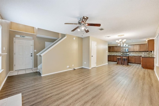 16504 Jadestone Dr, Leander, TX 78641 - unfurnished living room with light wood-style flooring, a chandelier, a ceiling fan, and stairs