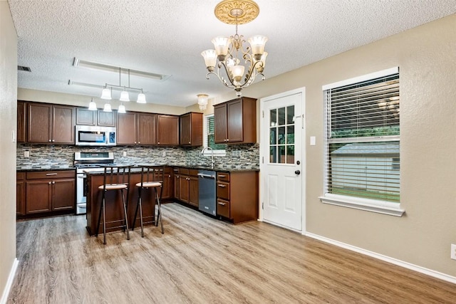 16504 Jadestone Dr, Leander, TX 78641 - kitchen featuring appliances with stainless steel finishes, a textured ceiling, light wood finished floors, dark countertops, and backsplash