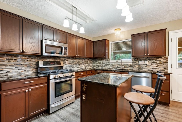 16504 Jadestone Dr, Leander, TX 78641 - kitchen with appliances with stainless steel finishes, light wood-style flooring, a textured ceiling, backsplash, and hanging light fixtures