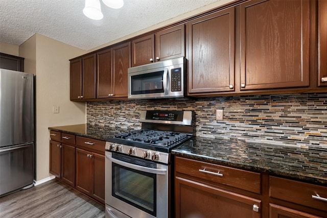 16504 Jadestone Dr, Leander, TX 78641 - kitchen featuring appliances with stainless steel finishes, light wood-style floors, dark stone countertops, tasteful backsplash, and a textured ceiling