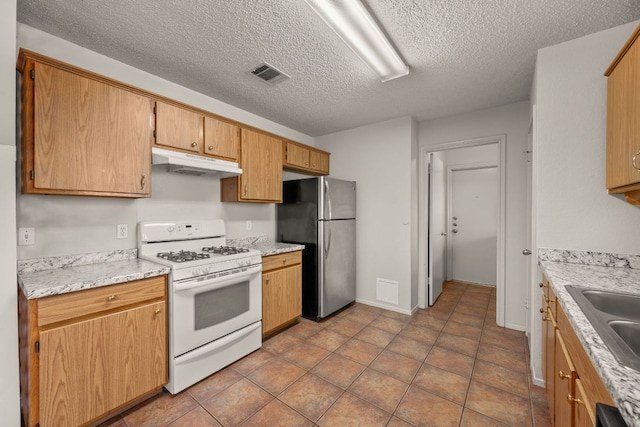 1625 Sylvia Ct, Round Rock, TX 78681 - kitchen with white gas range, under cabinet range hood, freestanding refrigerator, a textured ceiling, and light countertops