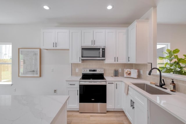 815 Fir Ln, Lockhart, TX 78644 - kitchen featuring appliances with stainless steel finishes, light stone counters, tasteful backsplash, white cabinets, and light wood-style floors