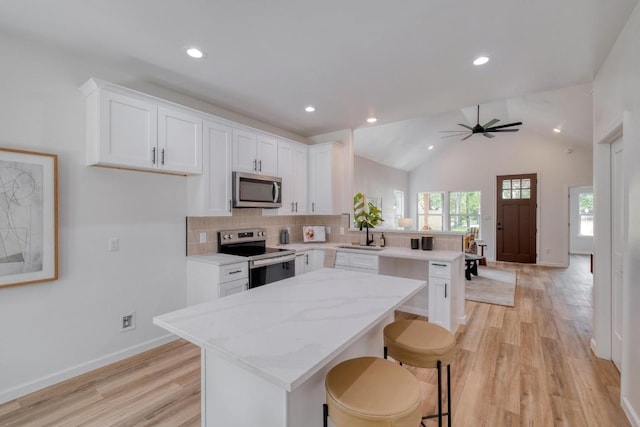 815 Fir Ln, Lockhart, TX 78644 - kitchen featuring stainless steel appliances, a peninsula, light wood finished floors, white cabinetry, and lofted ceiling