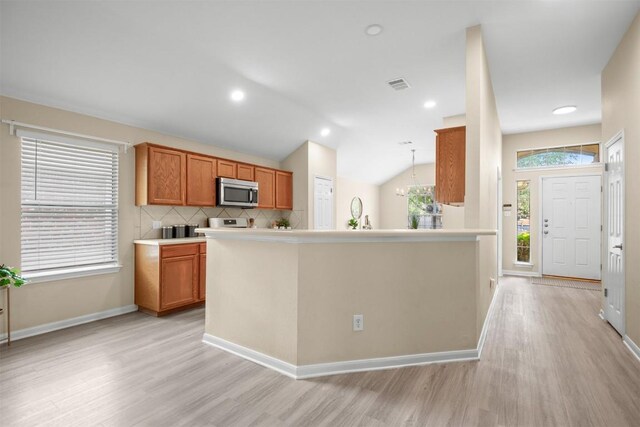 301 River Crossing Trl, Round Rock, TX 78665 - kitchen with stainless steel microwave, light wood-style floors, brown cabinetry, tasteful backsplash, and light countertops