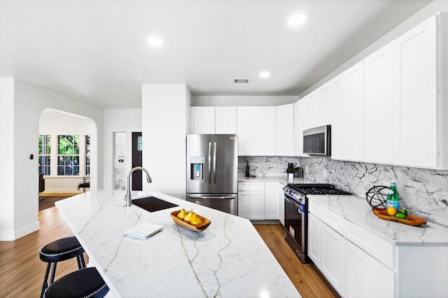 13305 Teton Ridge Cv, Austin, TX 78727 - kitchen with stainless steel appliances, arched walkways, tasteful backsplash, light wood-style floors, and white cabinetry