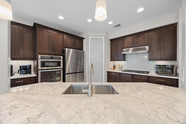 104 Atlanta Park Dr, Georgetown, TX 78628 - kitchen with appliances with stainless steel finishes, under cabinet range hood, dark brown cabinets, light stone countertops, and recessed lighting