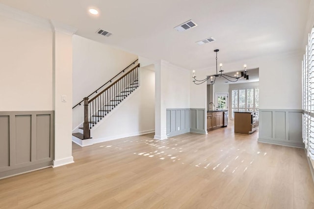 11108 Brista Way, Austin, TX 78726 - unfurnished living room with a chandelier, a decorative wall, stairs, light wood-style floors, and wainscoting