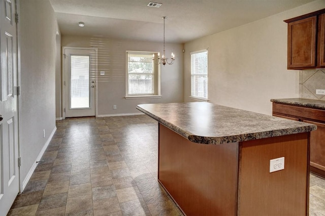 306 Grutsch Dr, Bastrop, TX 78602 - kitchen with a center island, a chandelier, brown cabinetry, decorative backsplash, and dark countertops