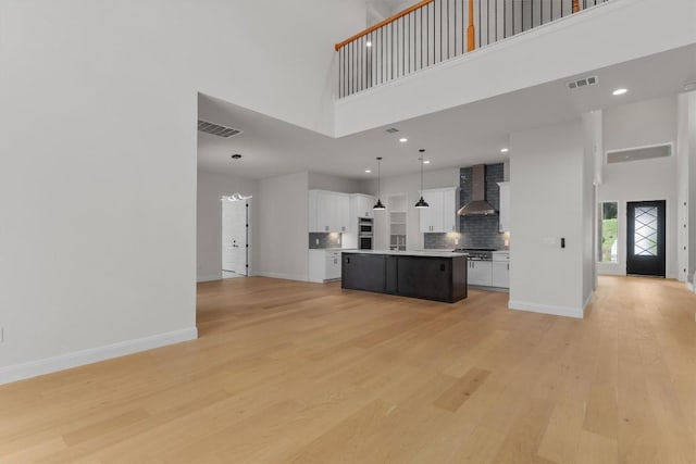 7705 Calcutta Run Dr, Jonestown, TX 78645 - kitchen featuring wall chimney range hood, open floor plan, a towering ceiling, light countertops, and light wood-style floors