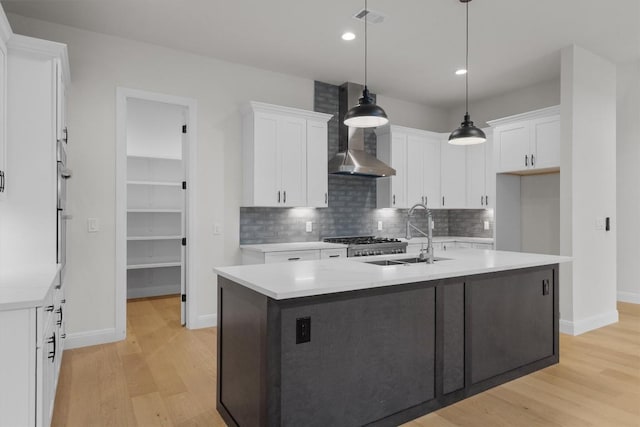 7705 Calcutta Run Dr, Jonestown, TX 78645 - kitchen featuring wall chimney exhaust hood, light wood-style floors, backsplash, white cabinets, and a center island with sink
