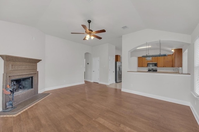109 Inman Dr, Hutto, TX 78634 - unfurnished living room featuring vaulted ceiling, arched walkways, a ceiling fan, light wood finished floors, and a fireplace with raised hearth