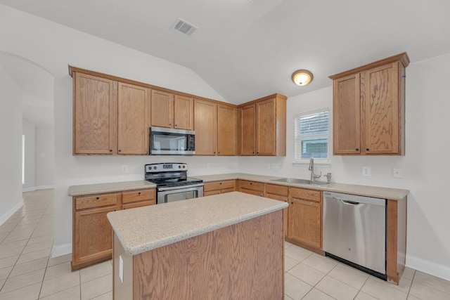 109 Inman Dr, Hutto, TX 78634 - kitchen featuring stainless steel appliances, lofted ceiling, light tile patterned floors, a kitchen island, and brown cabinetry