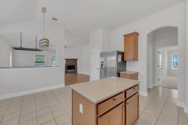 109 Inman Dr, Hutto, TX 78634 - kitchen featuring stainless steel fridge with ice dispenser, light tile patterned floors, arched walkways, a fireplace with raised hearth, and a kitchen island