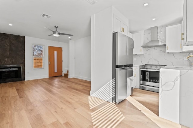 2706 Wheless Ln Unit 401, Austin, TX 78723 - kitchen featuring wall chimney exhaust hood, stainless steel appliances, light stone countertops, white cabinetry, and ceiling fan